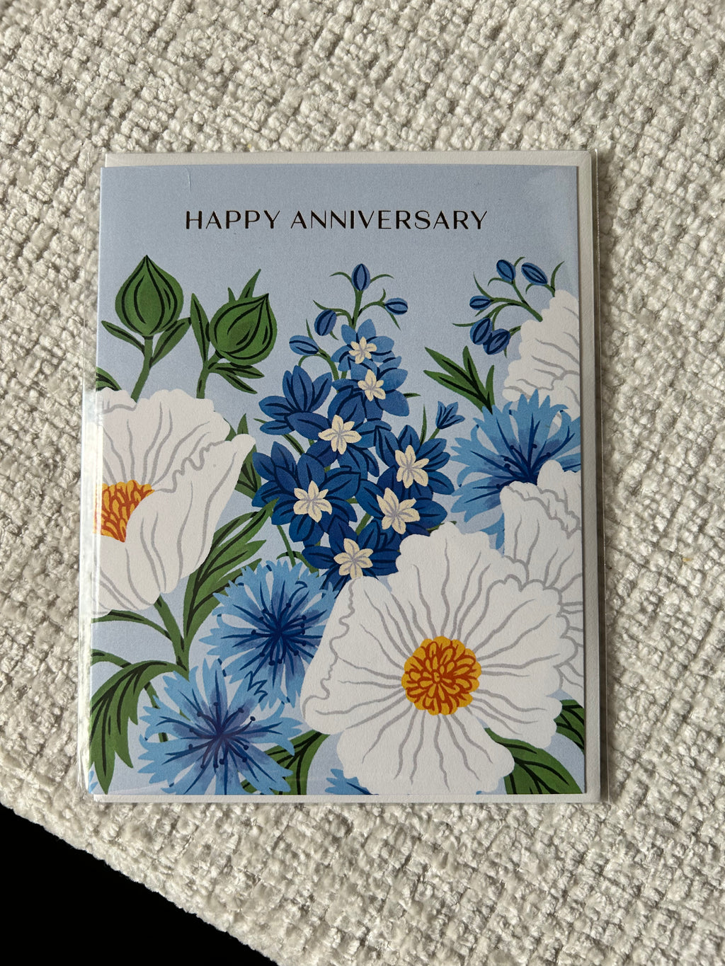 Floral anniversary greeting card featuring blue and white flowers on a soft blue background with the words "Happy Anniversary."