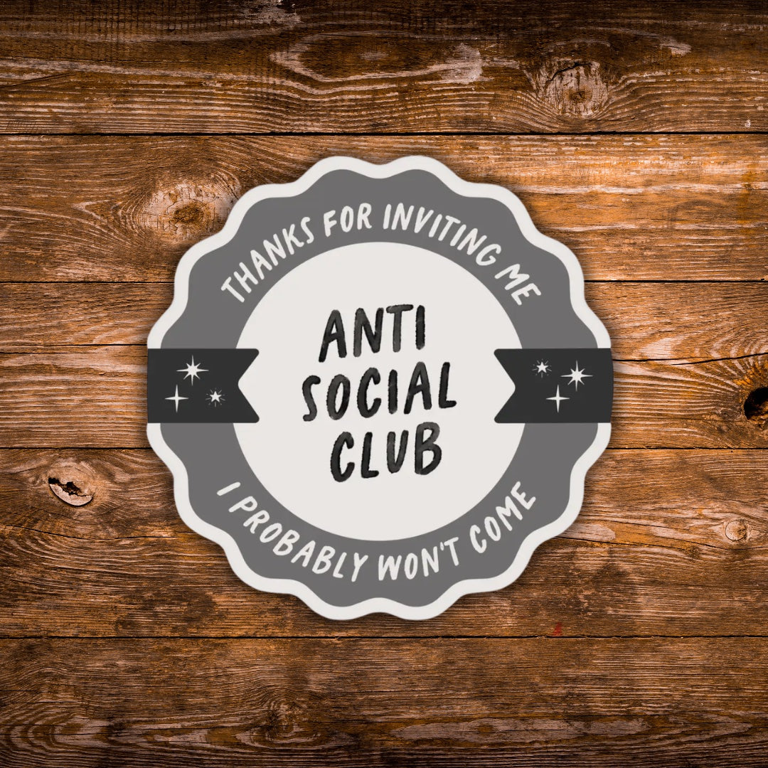 A scalloped circular sticker or decal with the text 'THANKS FOR INVITING ME I PROBABLY WON'T COME- ANTI SOCIAL CLUB' in black and gray lettering, shown on a rustic brown wood plank background.