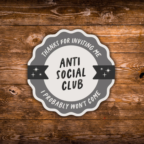 A scalloped circular sticker or decal with the text 'THANKS FOR INVITING ME I PROBABLY WON'T COME- ANTI SOCIAL CLUB' in black and gray lettering, shown on a rustic brown wood plank background.