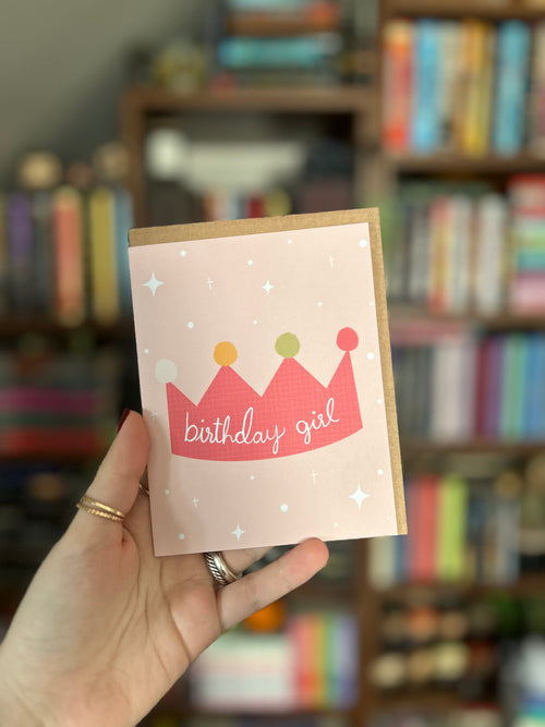 Cute birthday greeting card featuring a pink illustrated crown with the words "Birthday Girl" on a soft blush pink background with scattered stars.