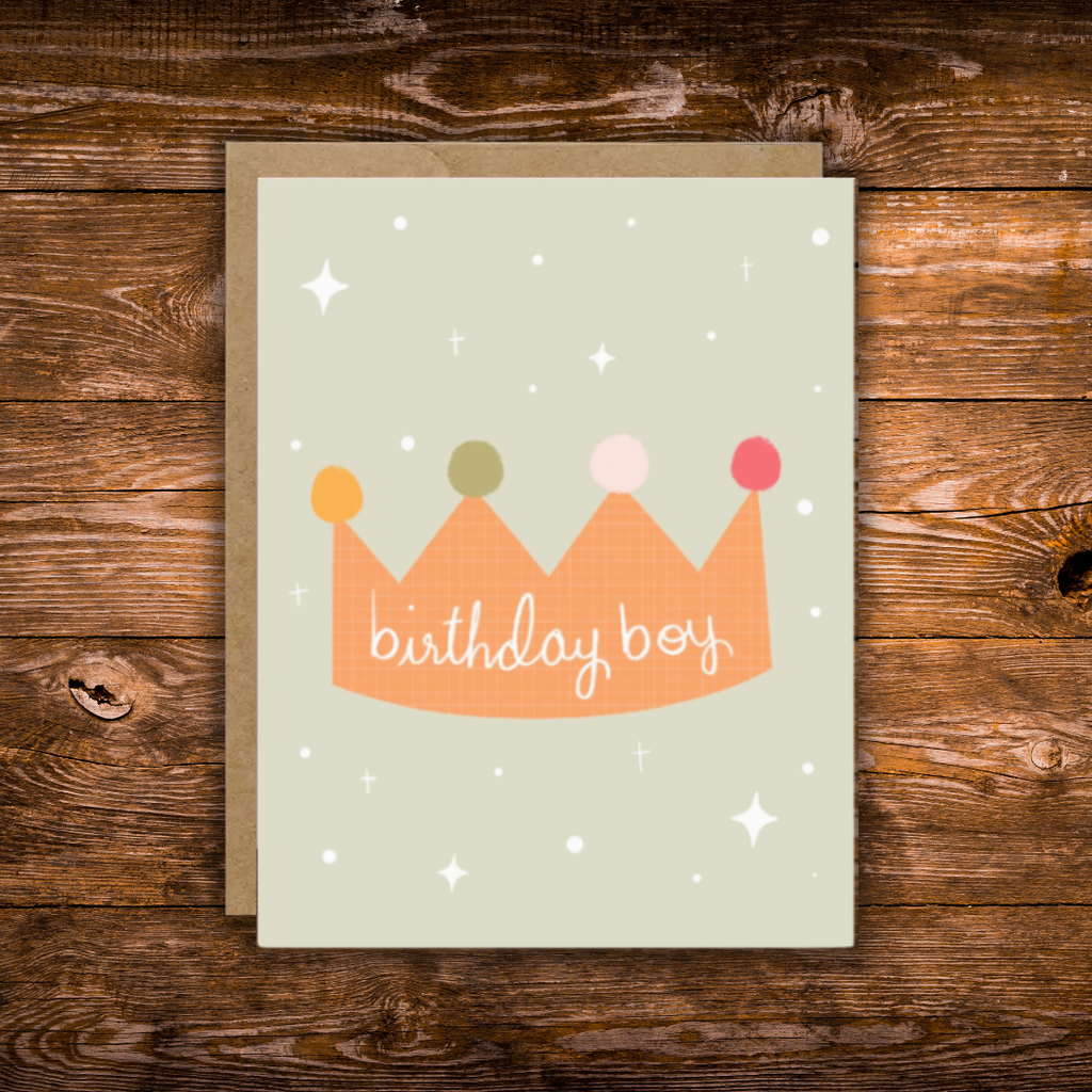 Cute birthday greeting card featuring a colorful illustrated crown with the words "Birthday Boy" on a soft sage green background with scattered stars.