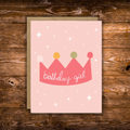 Cute birthday greeting card featuring a pink illustrated crown with the words "Birthday Girl" on a soft blush pink background with scattered stars.