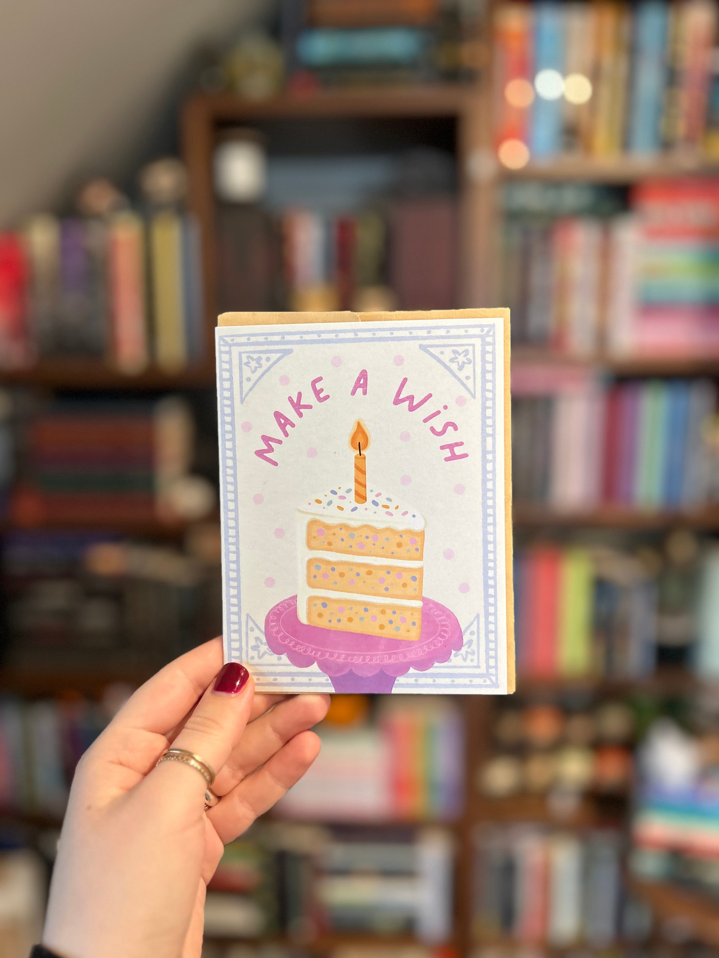 Pastel birthday greeting card featuring a slice of sprinkle cake with a lit candle and the words "Make a Wish."
