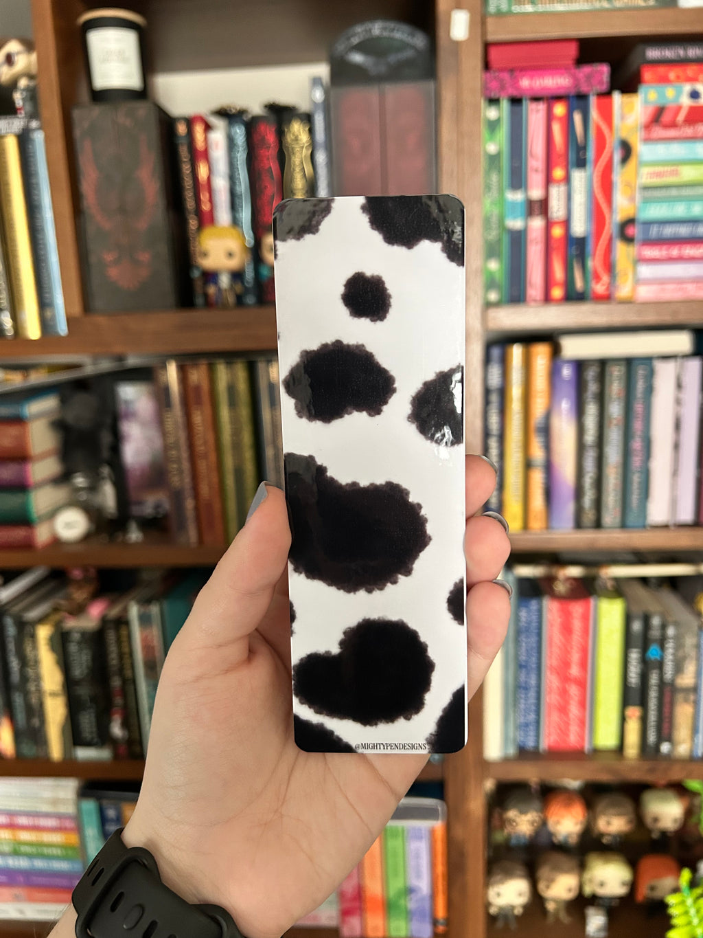 Double-sided cow bookmark featuring a rosy-cheeked white cow in a green grassy field with playful lettering, paired with a black-and-white cow print reverse.