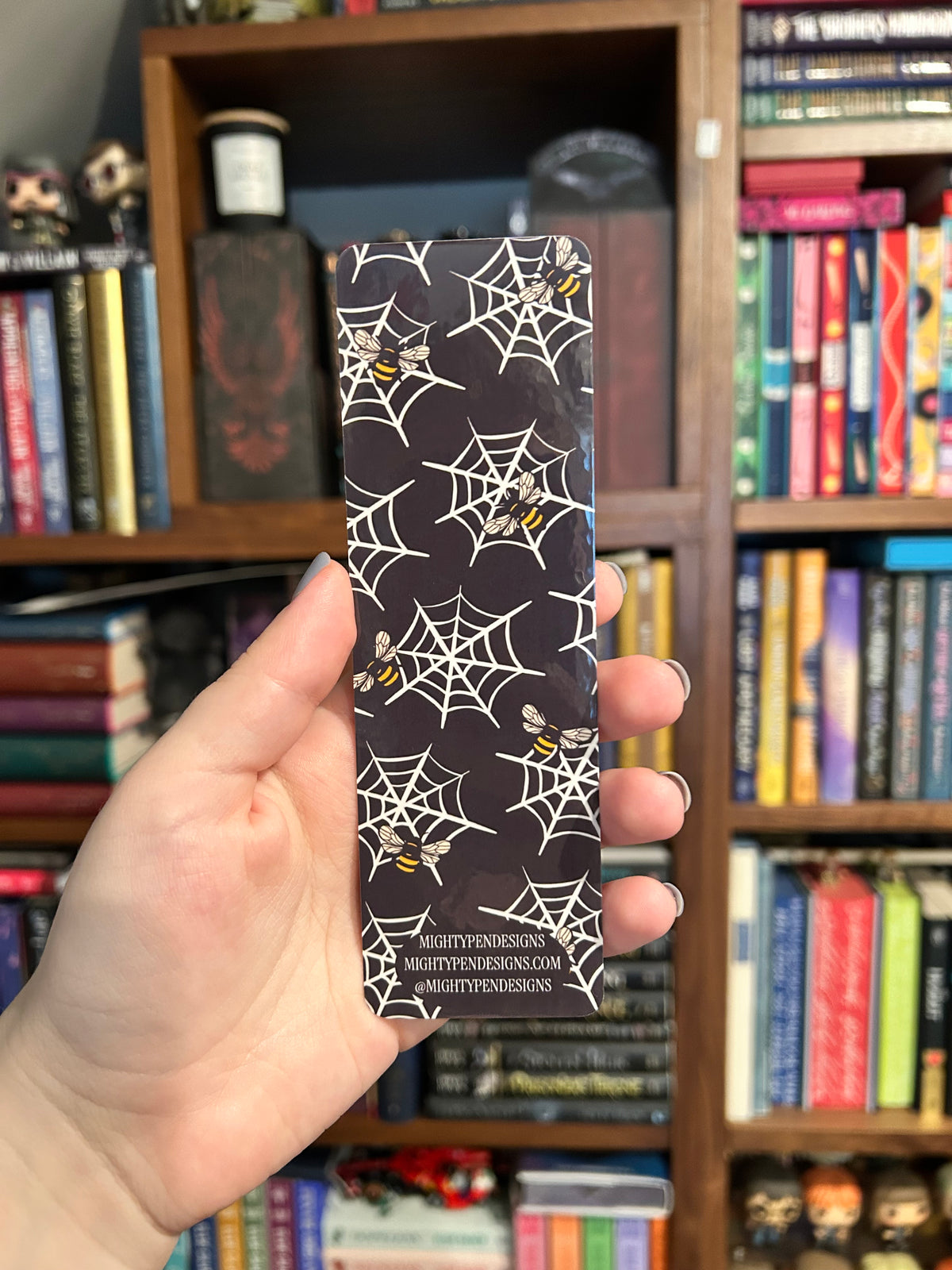 Double-sided gothic bookmark with skulls, black roses, candles, potion bottles, and golden accents on a cream background, paired with a black reverse featuring cream spiderwebs and golden bees.