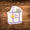 A die-cut sticker of a cream tote bag with lavender handles and trim, decorated with a yellow smiling sun charm, pink flowers, and the text 'Bag Lady'. The sticker is shown flat against a rustic brown wooden plank background.