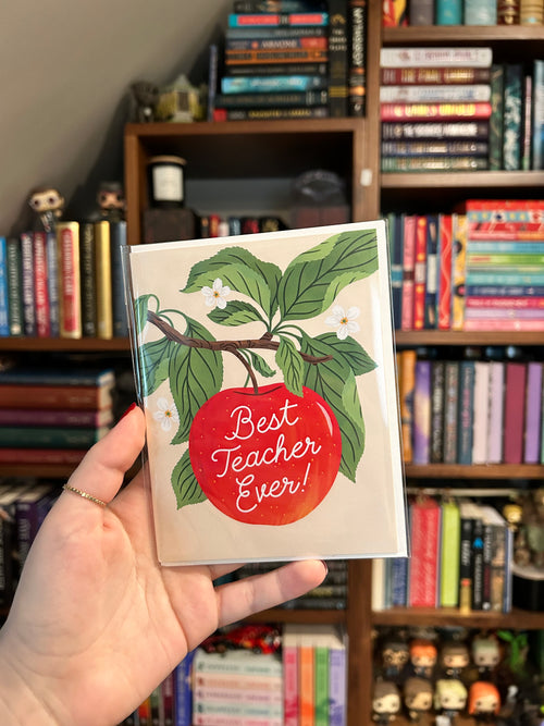 Teacher appreciation greeting card featuring a bright red apple hanging from a leafy branch with white blossoms and the words "Best Teacher Ever!" in white script.