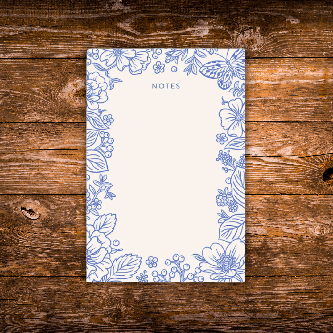 Decorative notepad featuring a delicate blue floral and butterfly border with a large blank writing area in the center on a cream background.