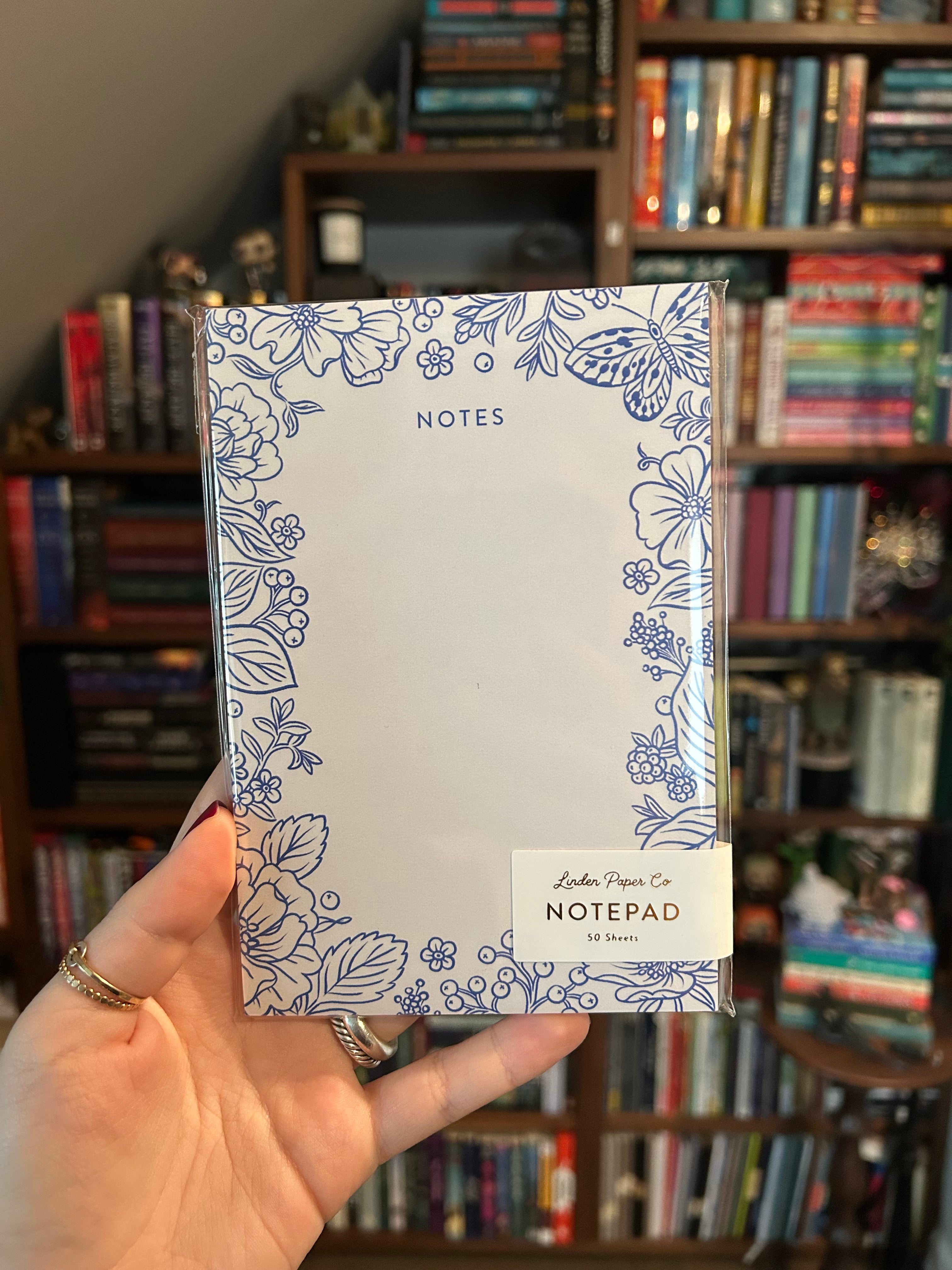 Decorative notepad featuring a delicate blue floral and butterfly border with a large blank writing area in the center on a cream background.