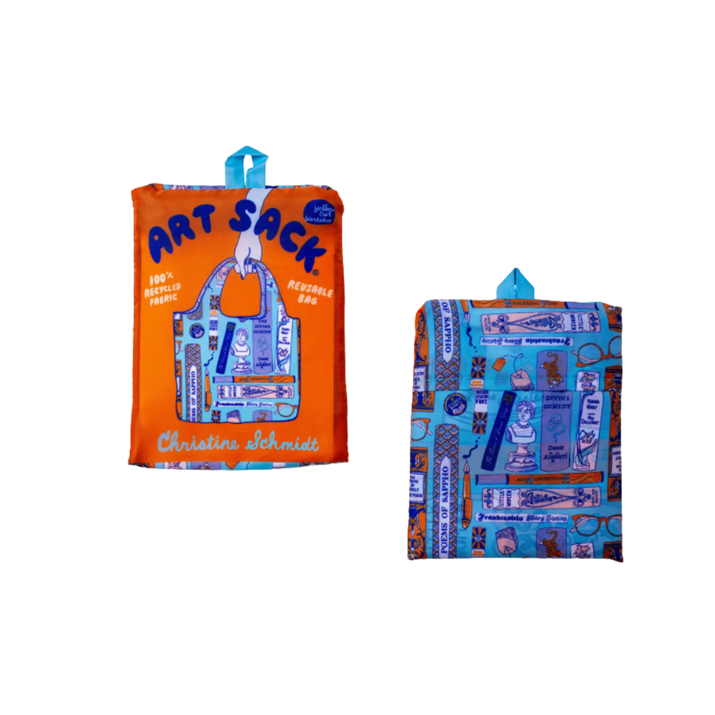 Reusable tote bag shown folded, with the front and back sides visible. The front features a bright orange background with navy “ART SACK” lettering, a blue-and-white literary-themed bag illustration, and the name “Christine Schmidt.” The back features the same blue-and-orange literary pattern, decorated with books, authors, writing and reading motifs, and other bookish illustrations.