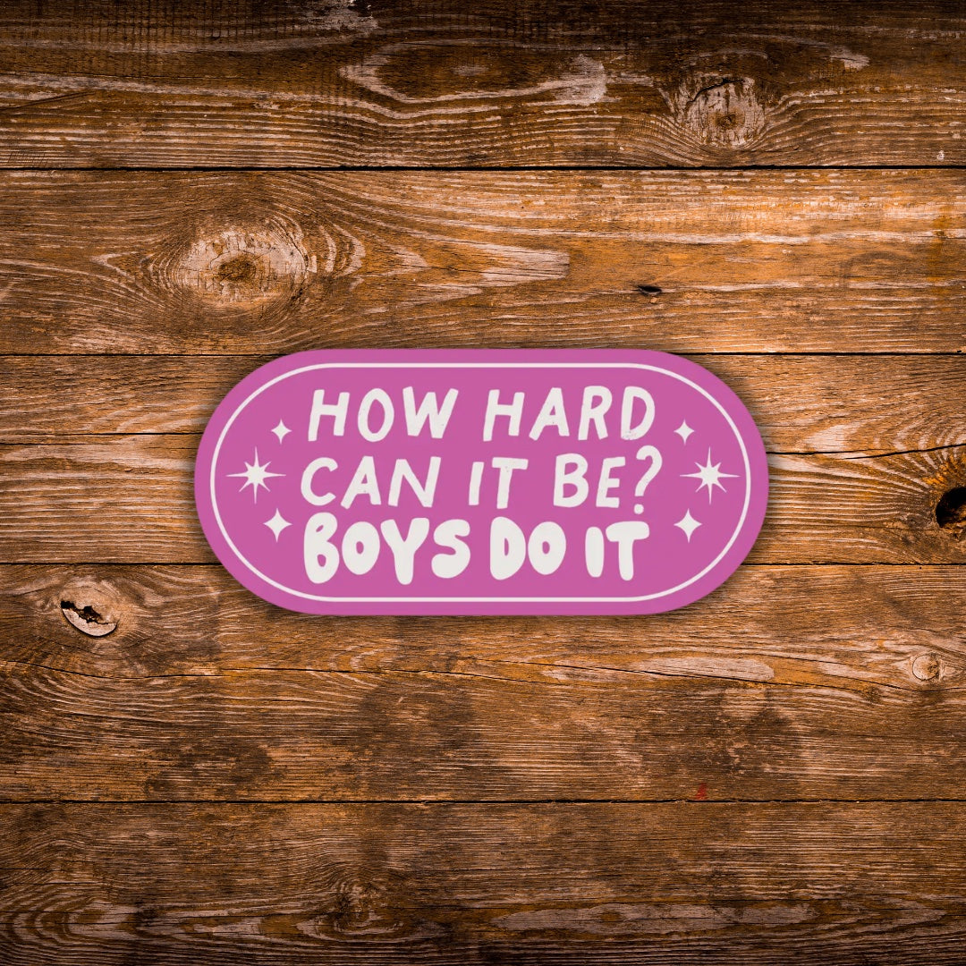 An oval pink sticker with white text reading 'HOW HARD CAN IT BE? BOYS DO IT' and small white star accents, shown on a rustic brown wooden plank background.