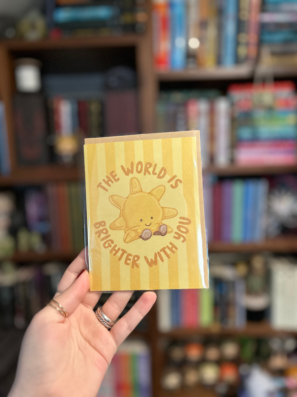Cute encouragement greeting card featuring a smiling sunshine with the message "The World Is Brighter With You" on a soft yellow striped background.