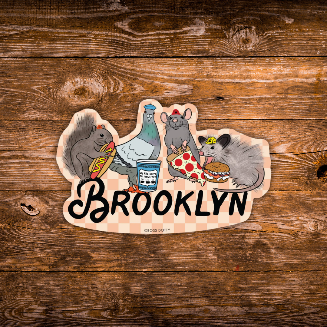 A die-cut sticker featuring cartoon animals and the word BROOKLYN, placed on a rustic brown wooden surface. The sticker shows a squirrel, a pigeon, a mouse, and a rat with food, above a pink-and-white checkered pattern and the word 'BROOKLYN' in black script.