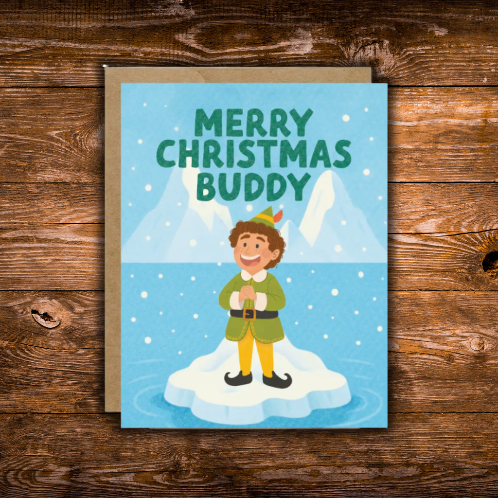 A Christmas greeting card with a kraft envelope, featuring the text 'MERRY CHRISTMAS BUDDY' and an illustration of an elf standing on a piece of ice in a snowy landscape. The card is displayed flat on a rustic wooden surface.