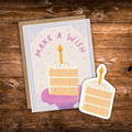 Matching birthday greeting card and waterproof vinyl sticker featuring a pastel slice of birthday cake with sprinkles, a lit candle, and the words "Make a Wish."