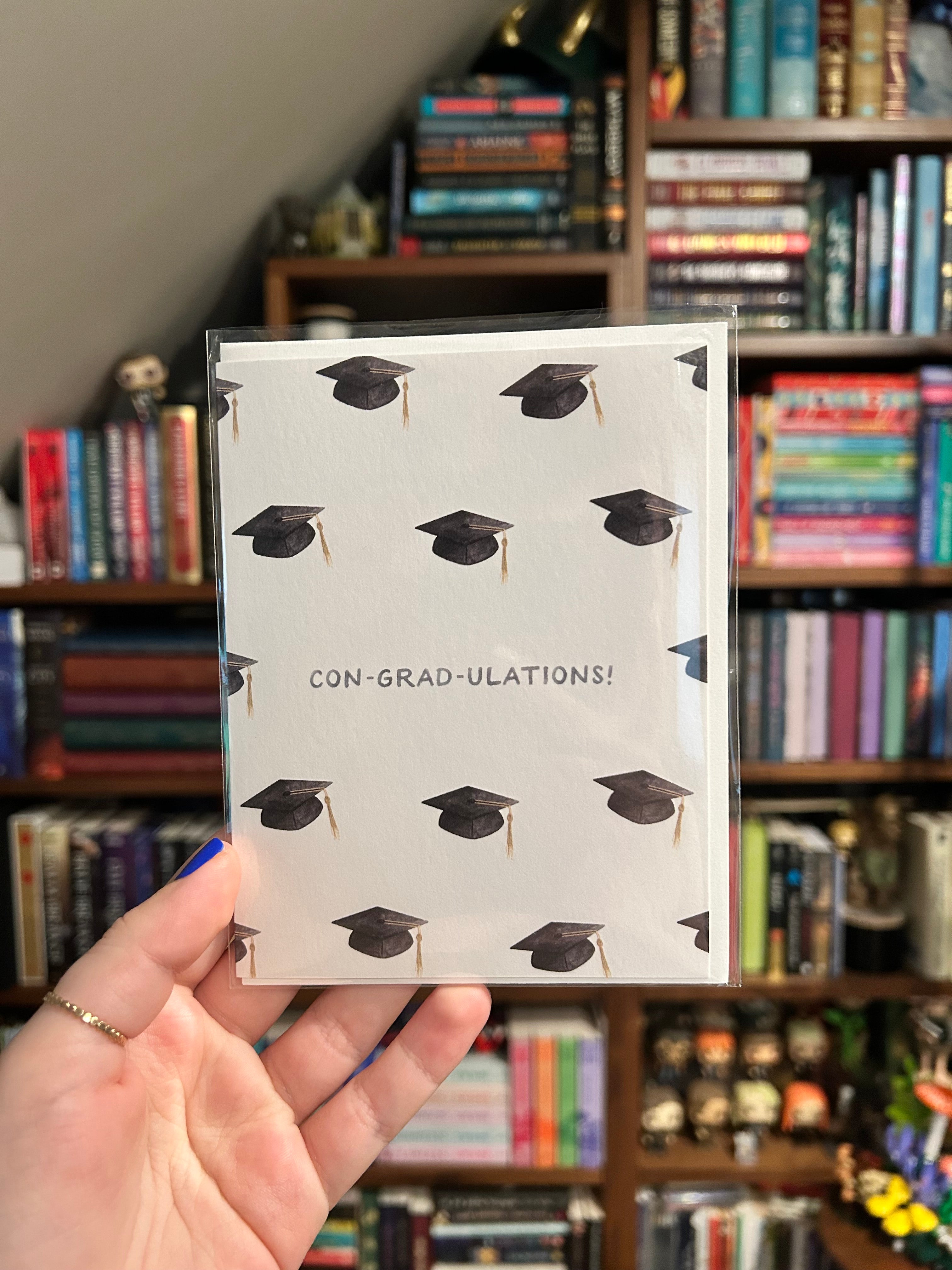 Graduation greeting card featuring a repeating pattern of graduation caps with the pun "Con-Grad-Ulations!" centered on a white background.