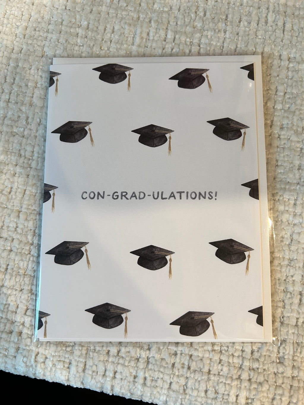 Graduation greeting card featuring a repeating pattern of graduation caps with the pun "Con-Grad-Ulations!" centered on a white background.