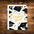 Graduation greeting card featuring black graduation caps, gold tassels, colorful confetti, and the words "Congrats Grad!" on a white background.