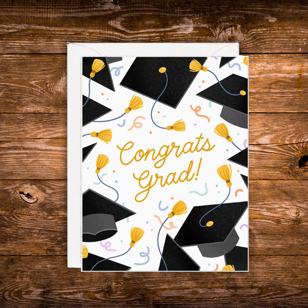 Graduation greeting card featuring black graduation caps, gold tassels, colorful confetti, and the words "Congrats Grad!" on a white background.