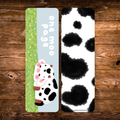 Double-sided cow bookmark featuring a rosy-cheeked white cow in a green grassy field with playful lettering, paired with a black-and-white cow print reverse.