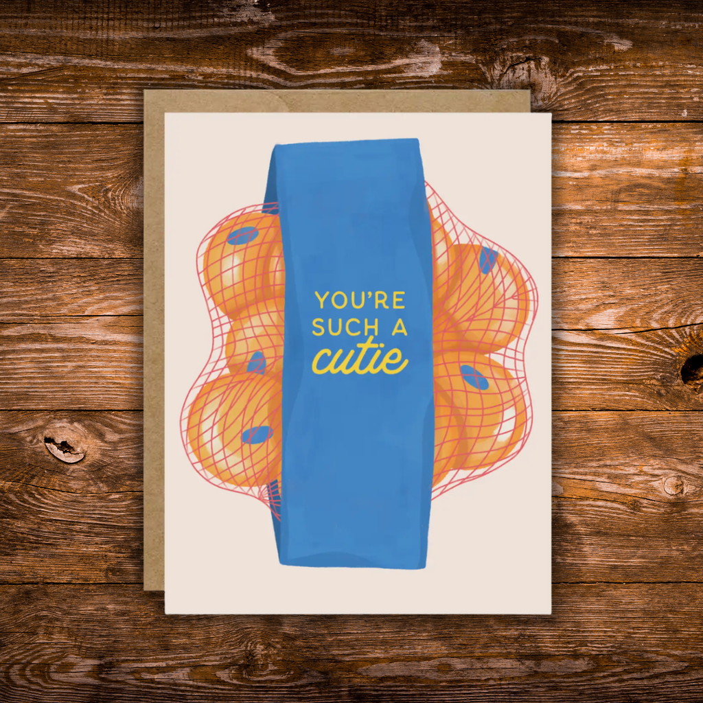Greeting card featuring a bag of clementines with the phrase "You're Such a Cutie" on a blue label against a neutral background.