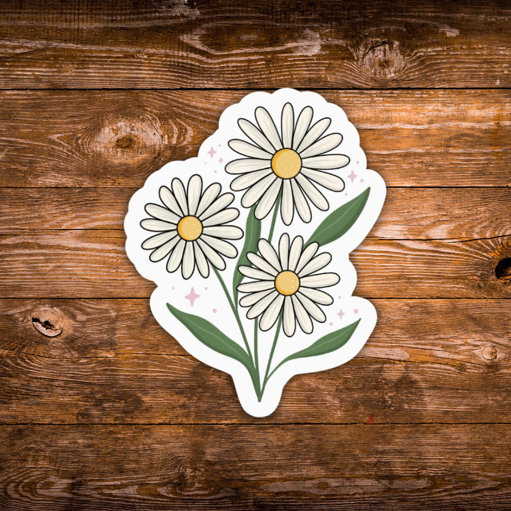 A die-cut sticker featuring three white daisy flowers with yellow centers and green stems, placed on a rustic brown wooden surface.