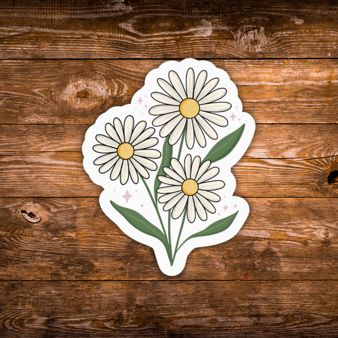 A die-cut sticker featuring three white daisy flowers with yellow centers and green stems, placed on a rustic brown wooden surface.