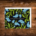 Landscape sympathy greeting card featuring blue forget-me-not flowers on a black background with the words "With Deepest Sympathy."