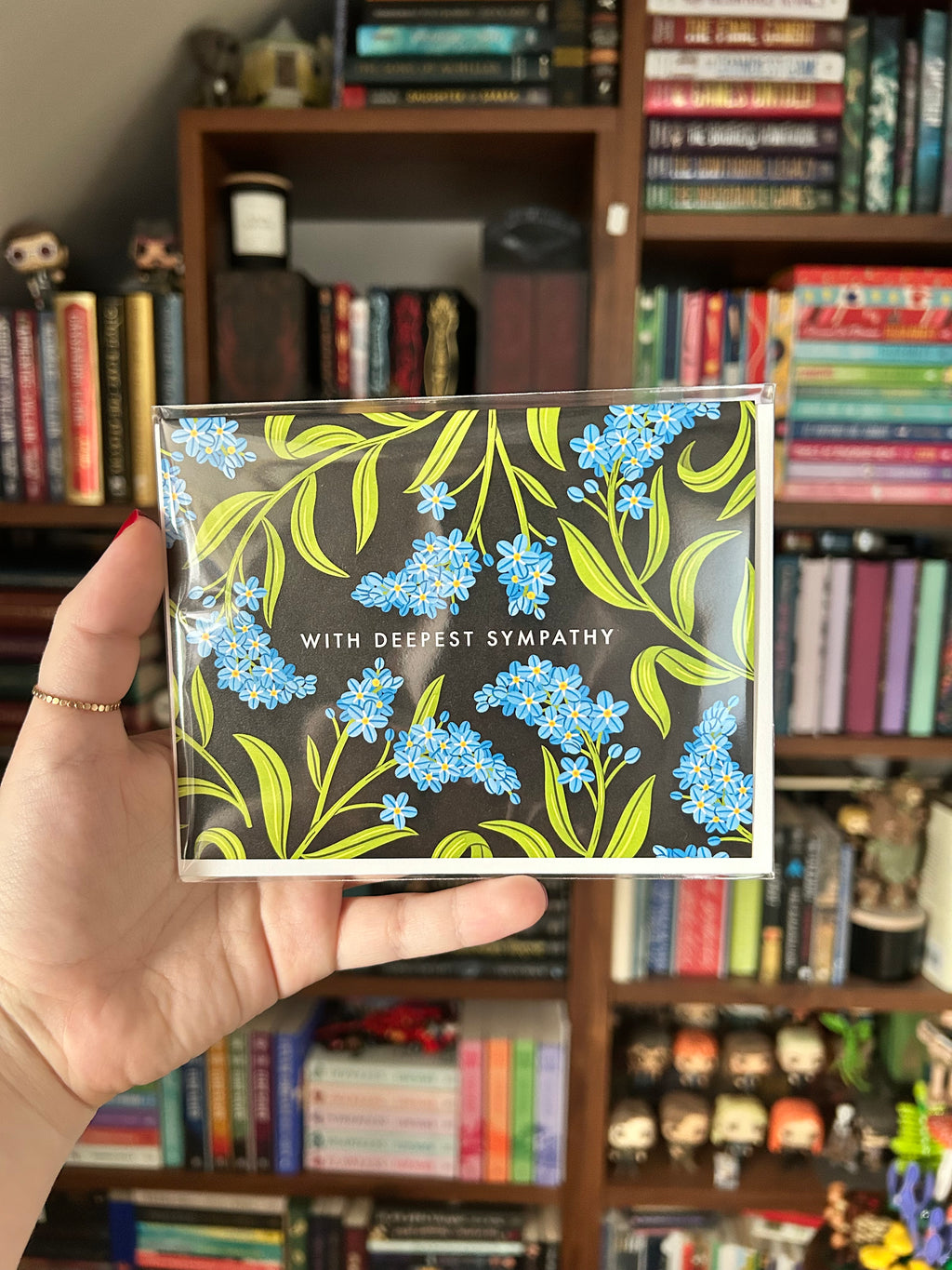 Landscape sympathy greeting card featuring blue forget-me-not flowers on a black background with the words "With Deepest Sympathy."