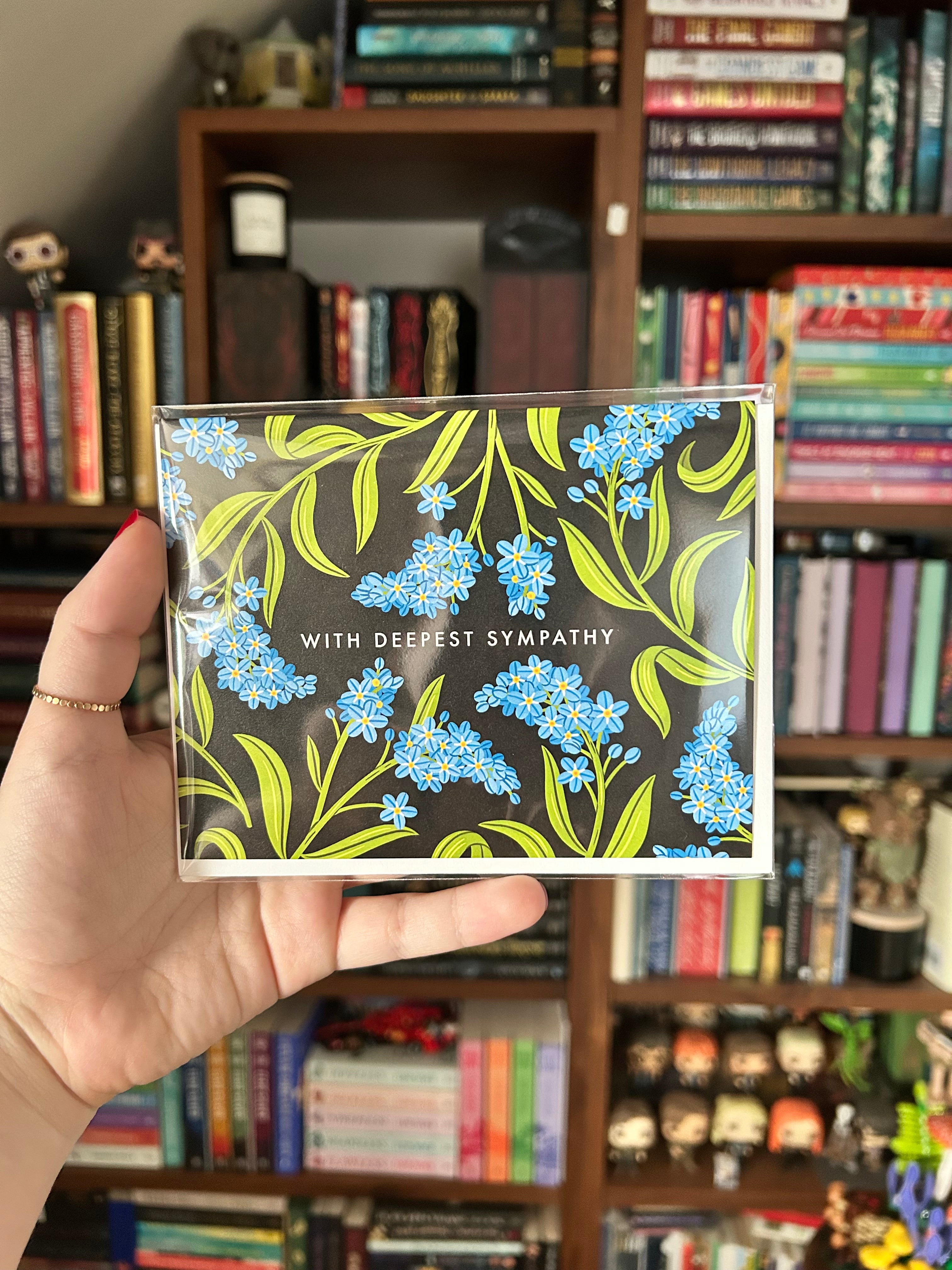 Landscape sympathy greeting card featuring blue forget-me-not flowers on a black background with the words "With Deepest Sympathy."