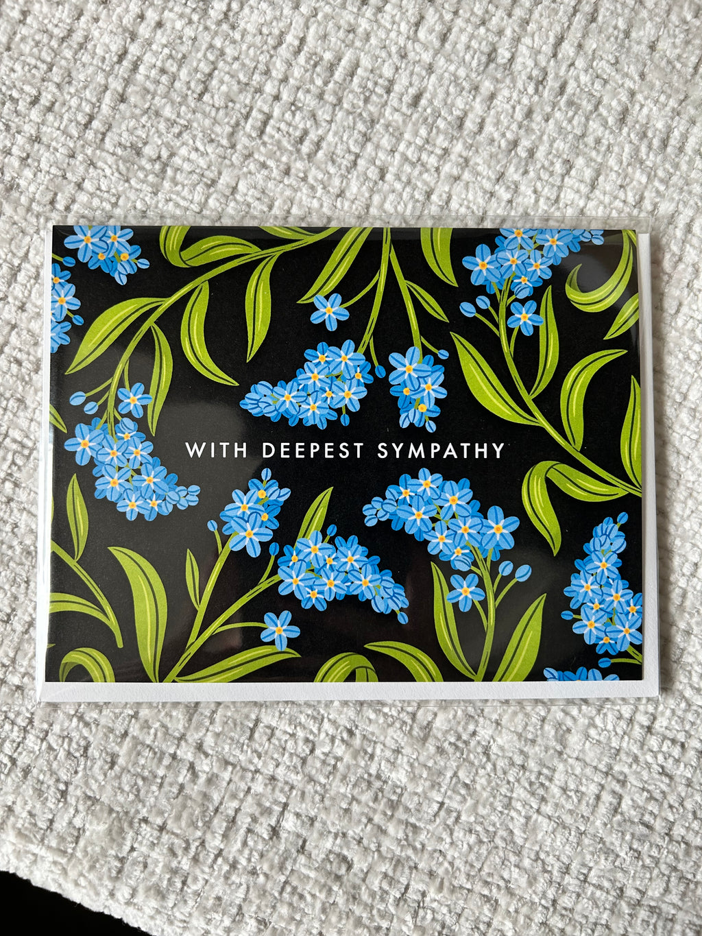 Landscape sympathy greeting card featuring blue forget-me-not flowers on a black background with the words "With Deepest Sympathy."