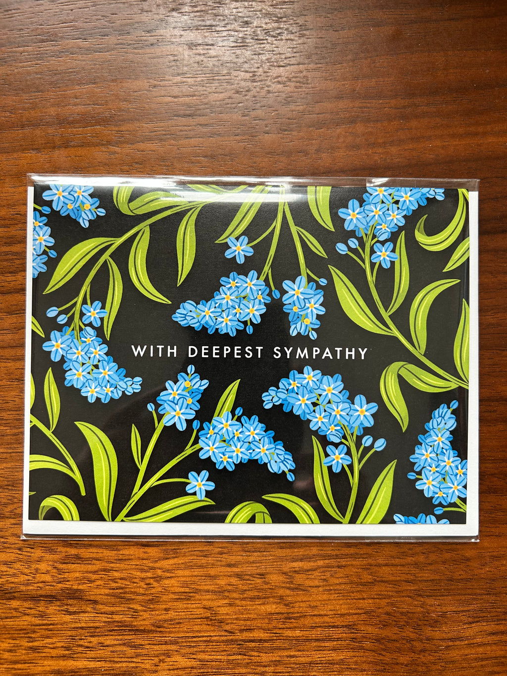 Landscape sympathy greeting card featuring blue forget-me-not flowers on a black background with the words "With Deepest Sympathy."