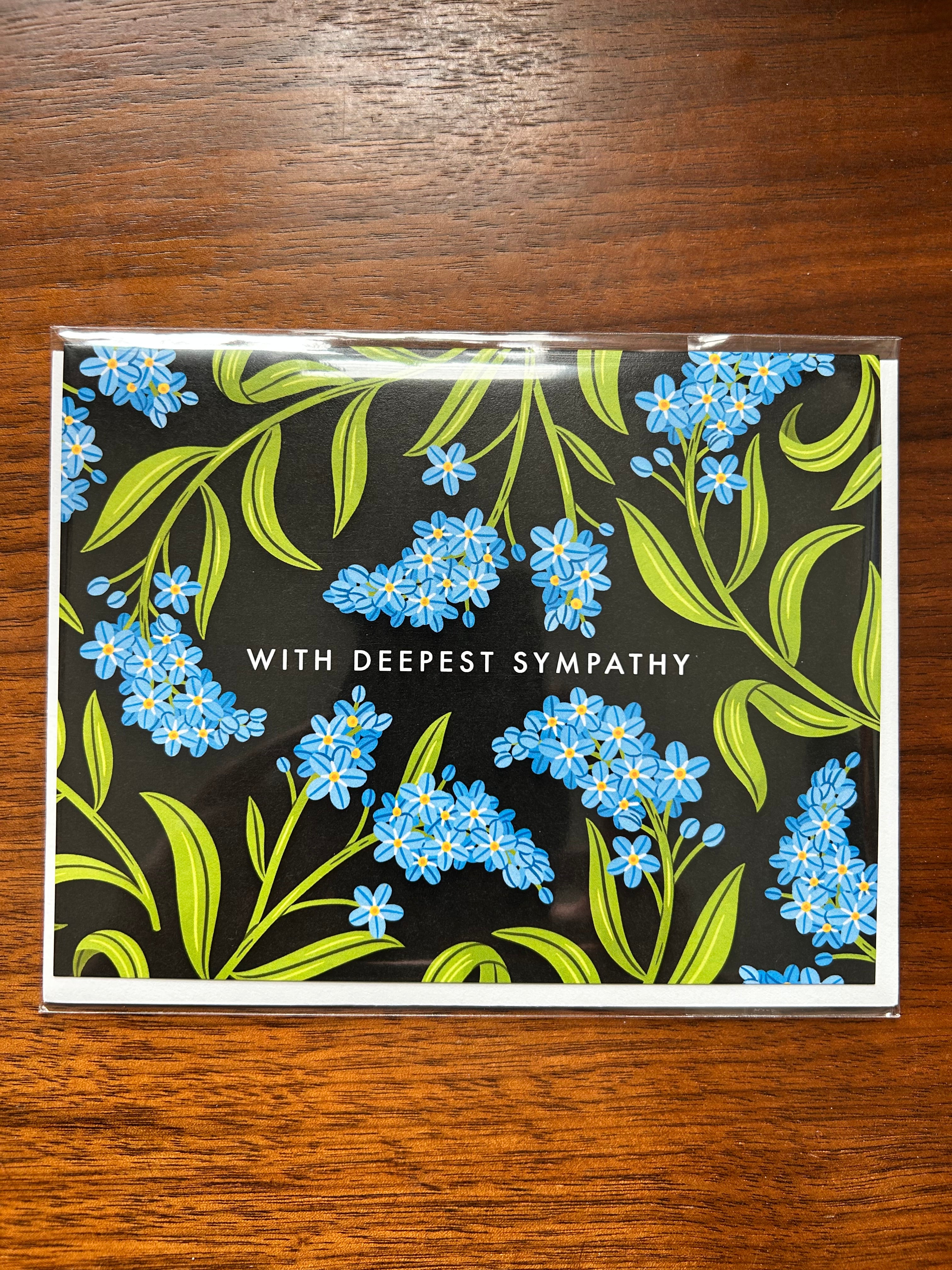 Landscape sympathy greeting card featuring blue forget-me-not flowers on a black background with the words "With Deepest Sympathy."