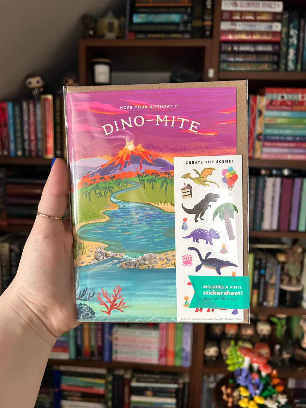 Interactive dinosaur birthday greeting card featuring a prehistoric landscape with an erupting volcano, river, and the message "Hope Your Birthday is Dino-Mite," plus a matching dinosaur-themed sticker sheet.