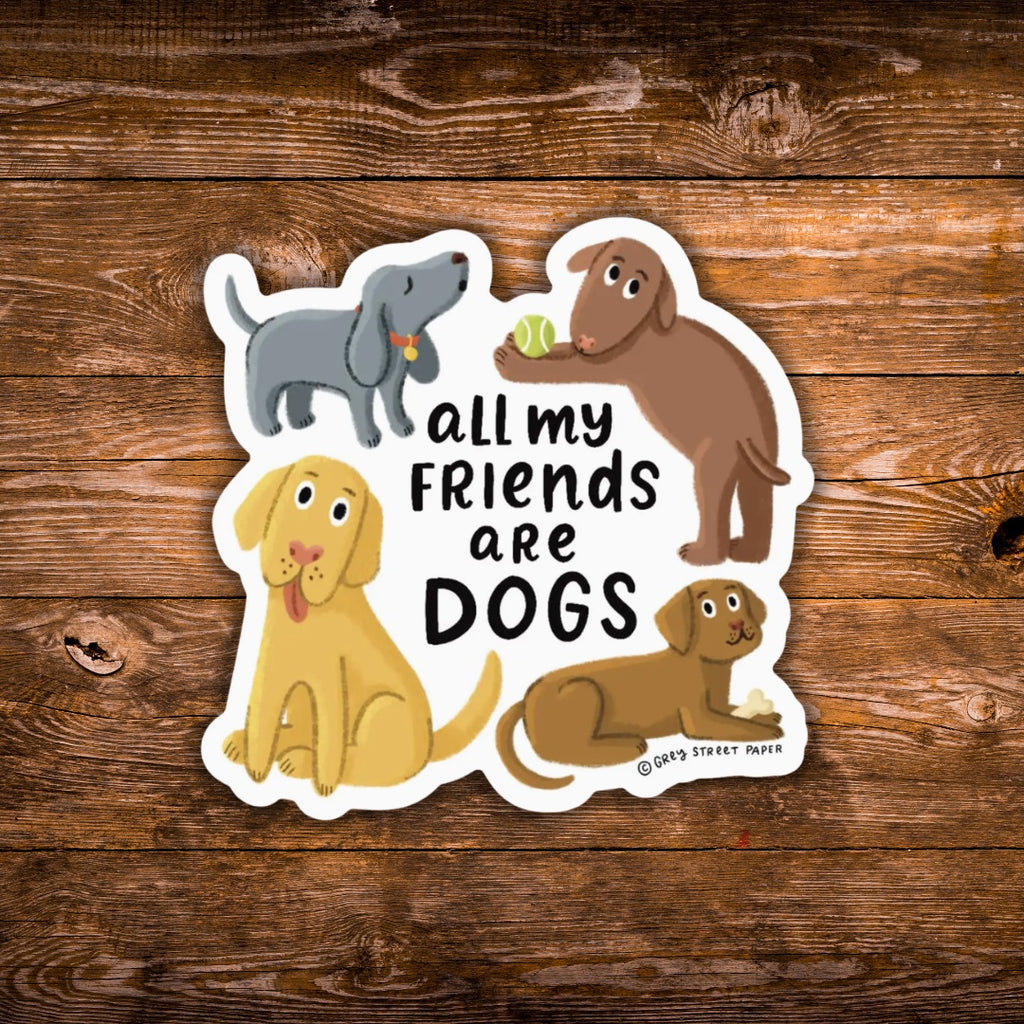 A die-cut sticker featuring cartoon dogs and the text 'all my FRIENDS are DOGS' on a white background, placed on a rustic brown wood plank surface. The sticker includes multiple dog illustrations in gray, brown, and yellow, with a small '©Grey Street Paper' credit at the bottom right.