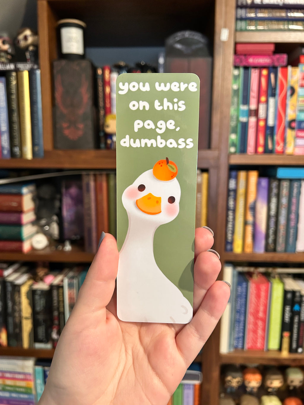 Double-sided bookmark featuring a white duck holding an orange and the phrase “You were on this page, dumbass,” with a green checkerboard and orange pattern on the reverse.