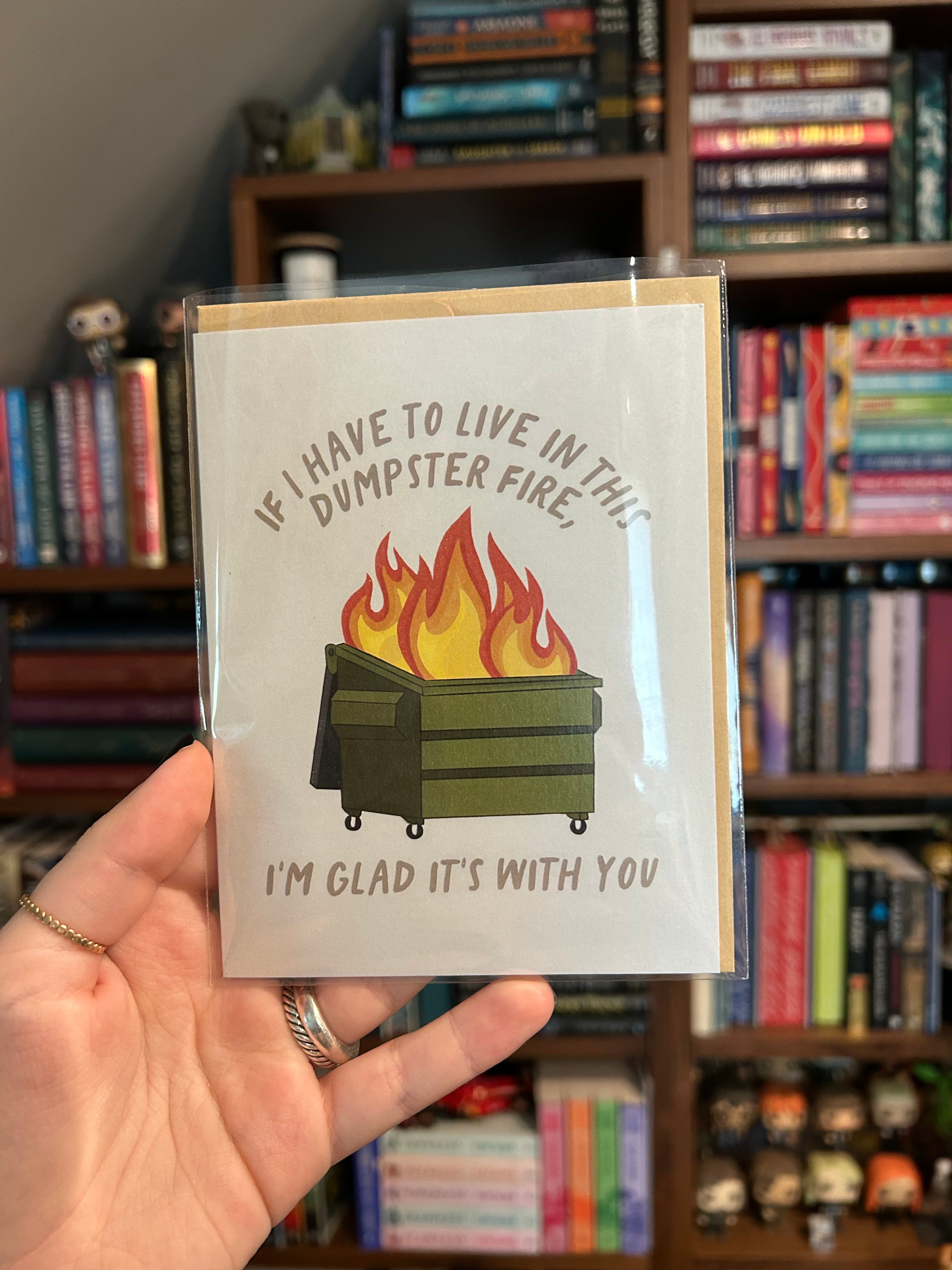 Funny greeting card featuring a flaming green dumpster with the message, "If I Have to Live in This Dumpster Fire, I'm Glad It's With You."