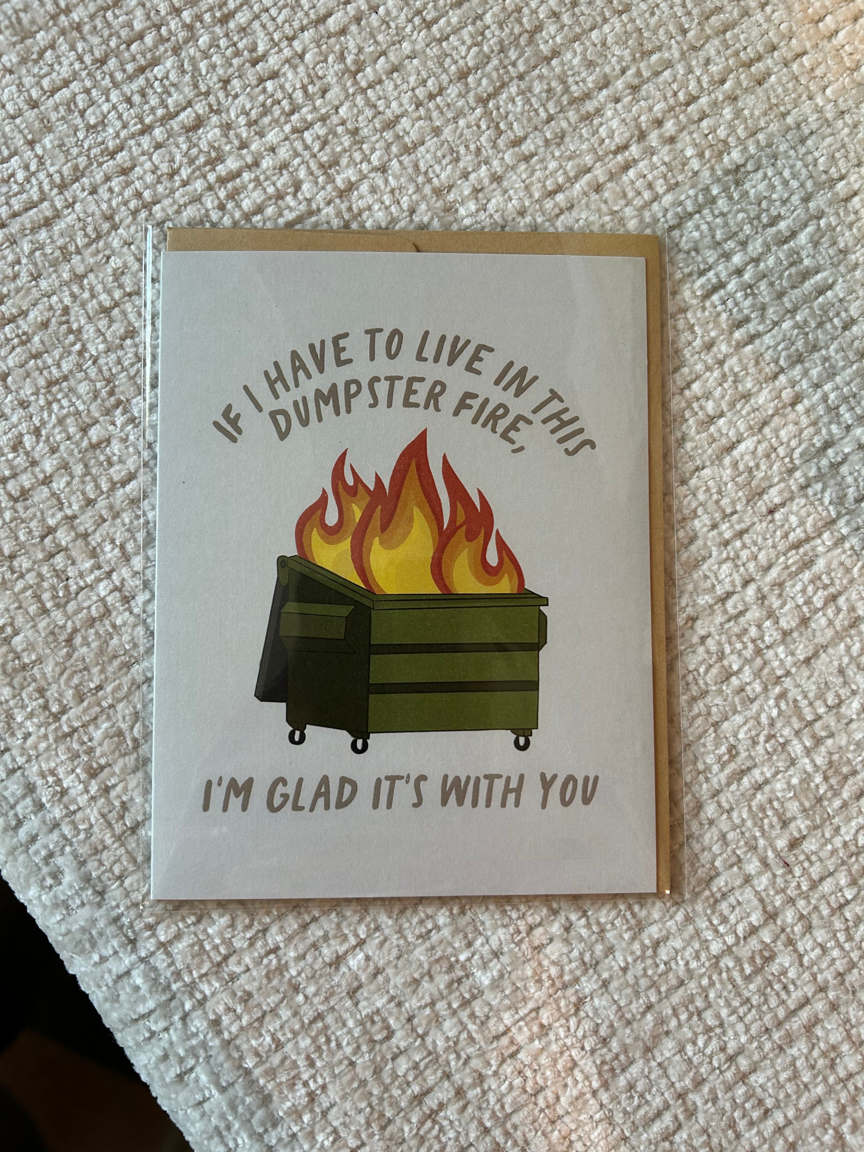 Funny greeting card featuring a flaming green dumpster with the message, "If I Have to Live in This Dumpster Fire, I'm Glad It's With You."