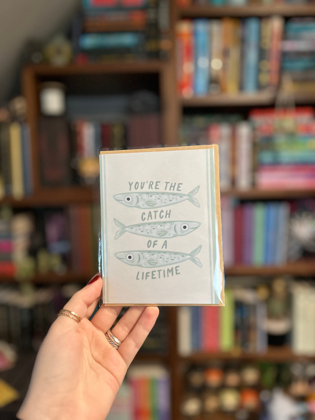 Cute romantic greeting card featuring three illustrated fish and the message "You're the Catch of a Lifetime" on a soft cream background with light blue accents.