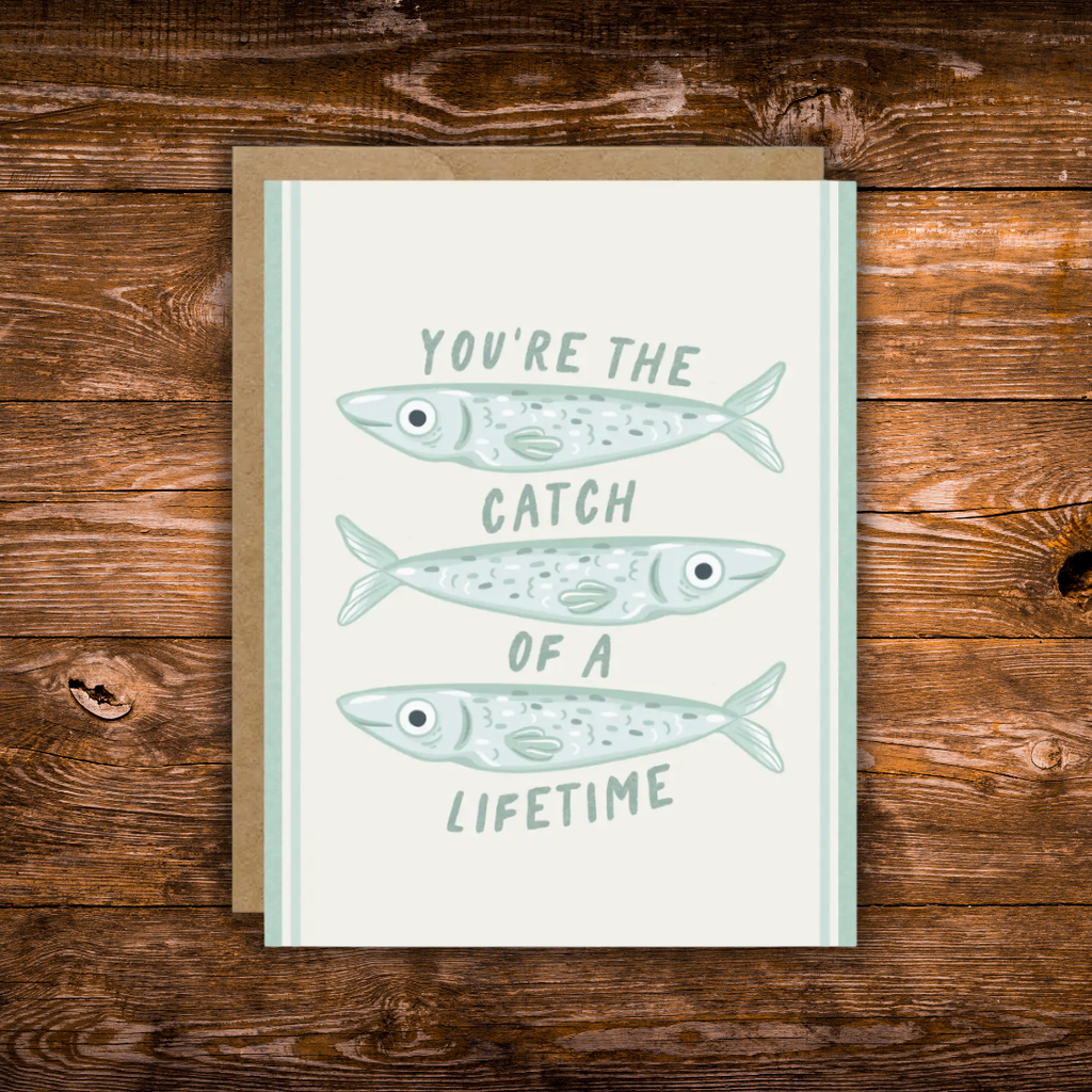 Cute romantic greeting card featuring three illustrated fish and the message "You're the Catch of a Lifetime" on a soft cream background with light blue accents.