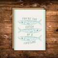 Cute romantic greeting card featuring three illustrated fish and the message "You're the Catch of a Lifetime" on a soft cream background with light blue accents.