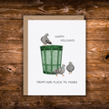 A white greeting card with a brown envelope, featuring a watercolor illustration of three pigeons around a green trash can, with the text 'HAPPY HOLIDAYS' and 'FROM OUR FLOCK TO YOURS', displayed on a rustic wooden background.