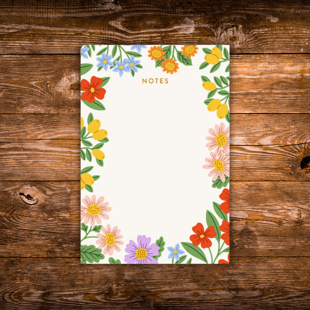 Decorative notepad featuring a colorful floral border with blooming flowers and greenery surrounding a large blank writing area on a cream background.