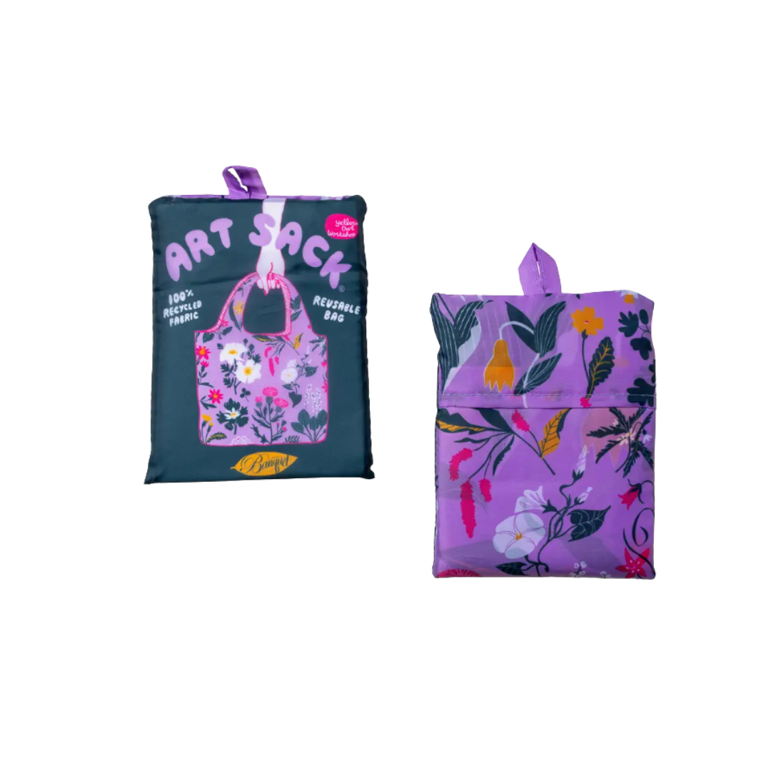 Reusable tote bag shown folded, with the front and back sides visible. The front features a dark teal background with pink “ART SACK” lettering and a floral-patterned reusable bag illustration. The back features a purple floral botanical pattern with a matching purple handle.