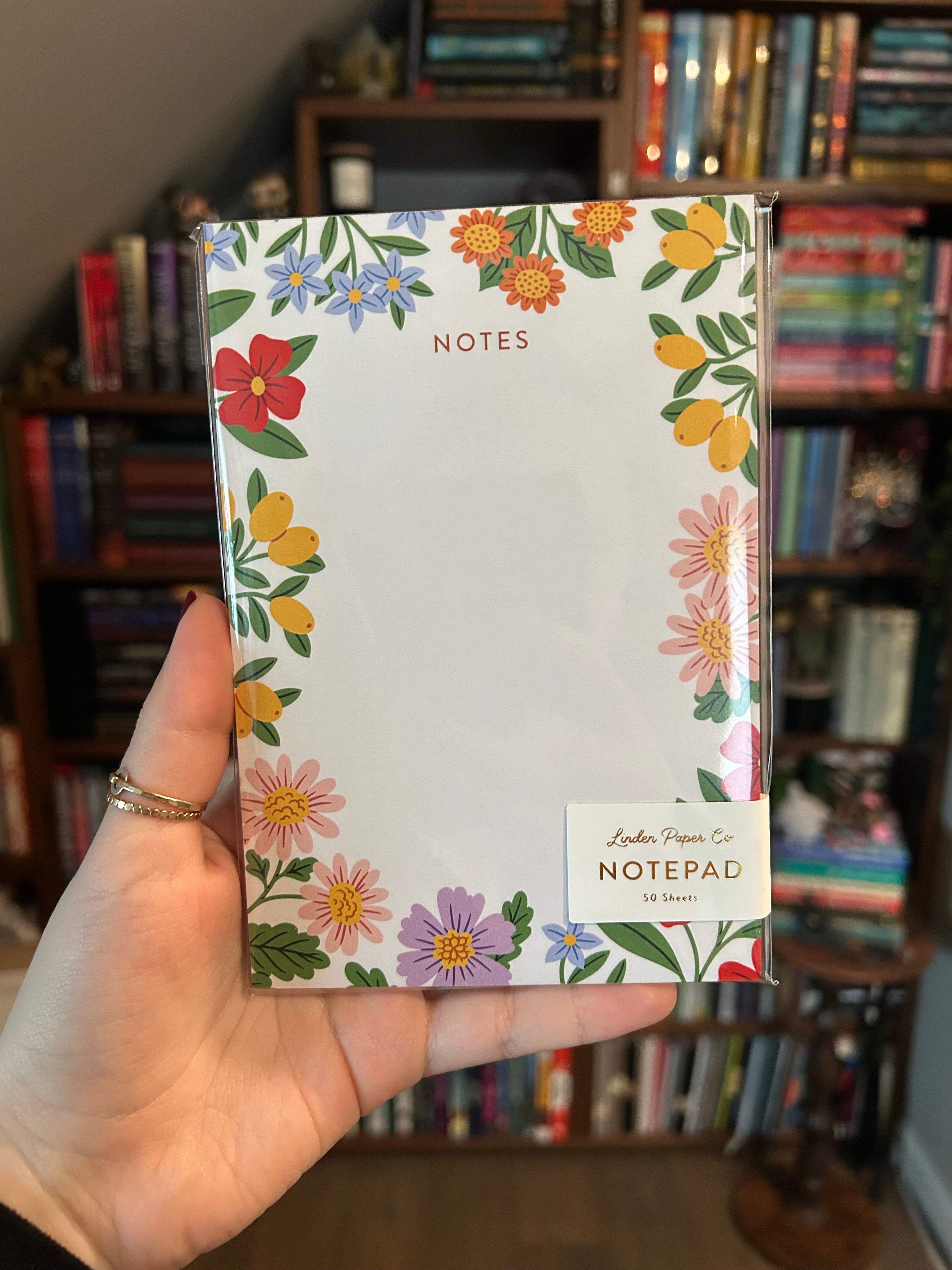 Decorative notepad featuring a colorful floral border with blooming flowers and greenery surrounding a large blank writing area on a cream background.