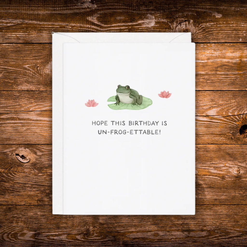 Birthday greeting card featuring a frog sitting on a lily pad with pink water lilies and the phrase "Hope This Birthday Is Un-Frog-Ettable!"