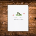 Birthday greeting card featuring a frog sitting on a lily pad with pink water lilies and the phrase "Hope This Birthday Is Un-Frog-Ettable!"