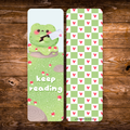 Double-sided frog bookmark featuring a cute green frog holding a cleaver in a mushroom-covered woodland scene with “Keep Reading” lettering, paired with a green checkerboard pattern and pink hearts.