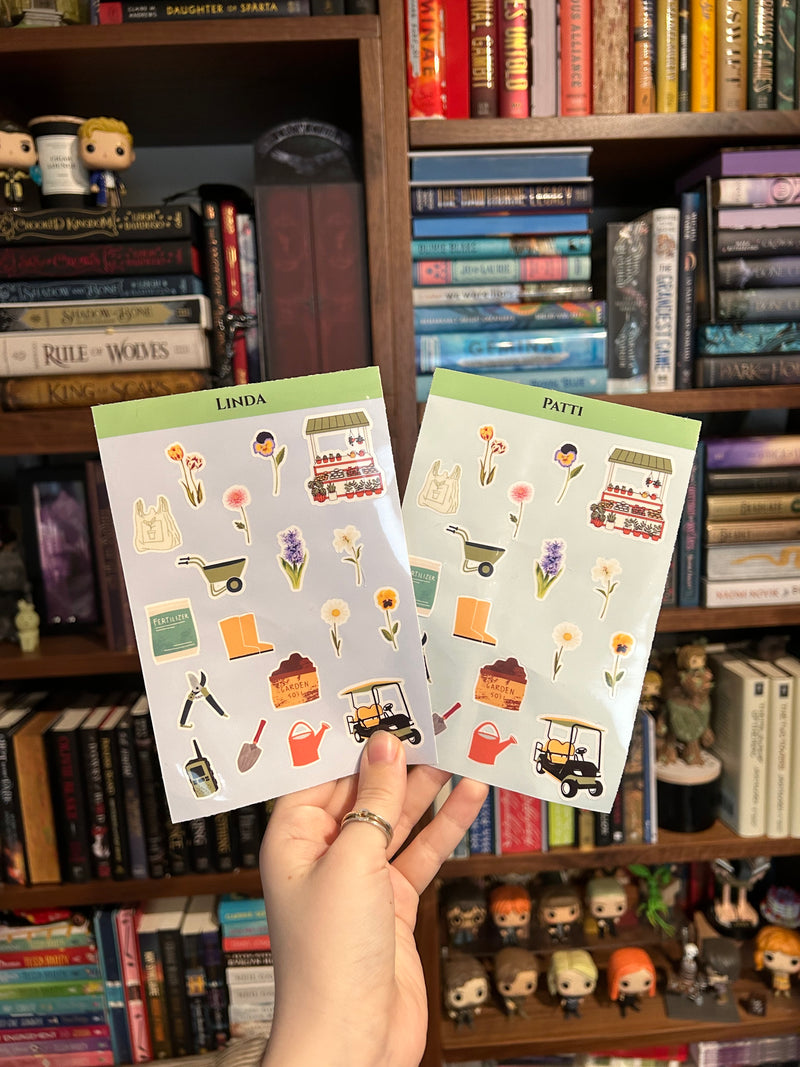 Two sticker sheets held up by a hand in front of a bookshelf. The sheets have green headers reading 'LINDA' and 'PATR' and are decorated with small illustrated stickers including flowers, golf carts, a cart, and gardening items.
