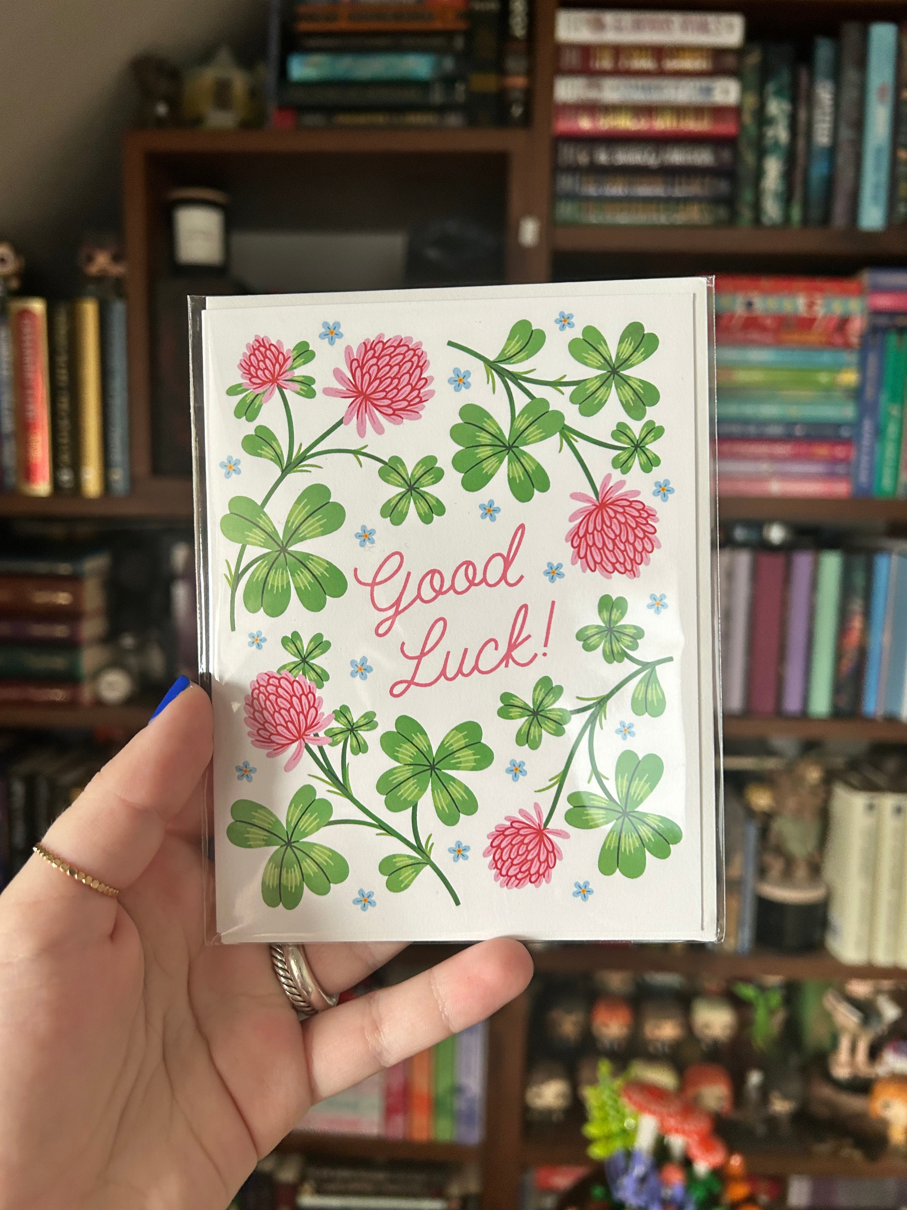 Good luck greeting card featuring green clovers, pink flowers, and the words "Good Luck!"